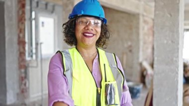 Genç, güzel Latin kadın inşaatçı, gülümsüyor. İnşaat alanında kendine güveniyor.