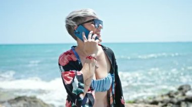 Bikini ve güneş gözlüğü takan genç bir turist kumsalda akıllı telefondan konuşuyor.