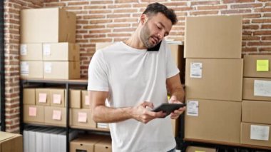 Latin kökenli genç iş adamı ofisteki dokunmatik bilgisayarla akıllı telefondan konuşuyor.