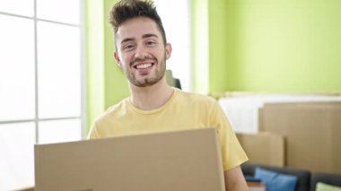 Young hispanic man smiling confident holding fragile package at new home