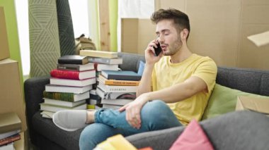 Genç İspanyol bir adam akıllı telefonuyla konuşuyor. Yeni evinde koltukta oturmuş kutlama yapıyor.