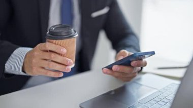 Genç İspanyol iş adamı akıllı telefon kullanıyor. Ofiste kahve içiyor.