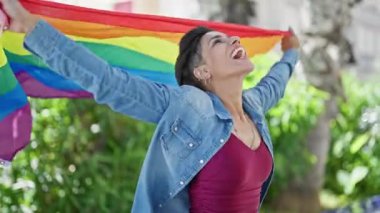 Genç, güzel İspanyol kadın gülümsüyor. Elinde gökkuşağı bayrağı var. Parkta kendi kendine dönüyor.