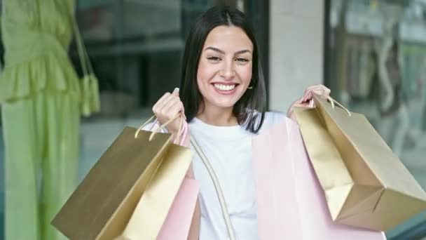 若い美しいヒスパニック女性笑顔行くショッピングバッグで衣料品店 — ストック動画