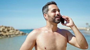 Genç İspanyol turist akıllı telefondan konuşuyor plajda üstsüz duruyor.
