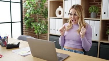 Genç, güzel İspanyol iş kadını laptopunu kullanarak ofiste kazanan ifadeyle çalışıyor.