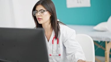 Genç beyaz kadın doktor klinikte telefonla konuşurken bilgisayar kullanıyor.