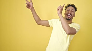 Afro-Amerikalı adam parmaklarını kenarı işaret ederek izole edilmiş sarı arka planda dans ediyor.