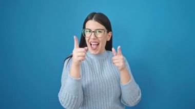 Genç İspanyol kadın gülümsüyor. Kendine güveni tam, mavi arka planda kamerayı işaret ediyor.