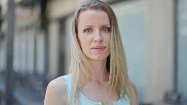 Young blonde woman smiling confident combing hair with hand at street