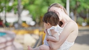 Anne ve kızı parkta birbirlerine gülümsüyorlar.