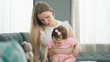 Anne ve kızı kanepede oturup birbirlerine sarılıp baş parmak hareketlerini yapıyorlar.