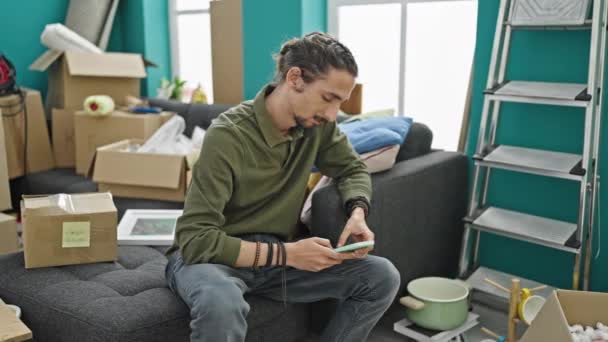 Hombre Hispano Joven Usando Teléfono Inteligente Sentado Sofá Nuevo Hogar — Vídeos de Stock