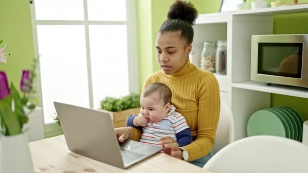 母親と息子はオンラインで働いているテーブルの上に座っている間ケア赤ちゃんはダイニングルームで — ストック動画