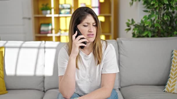 年轻的金发女人在智能手机上说话 在家里看起来很不高兴 — 图库视频影像