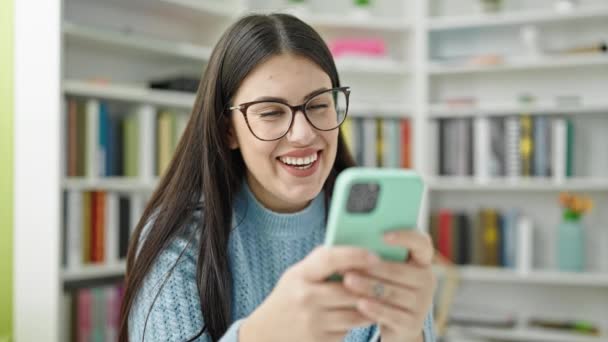 Kütüphanede Akıllı Telefon Kullanarak Gülümseyen Genç Spanyol Bayan Öğrenci — Stok video