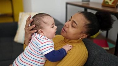 Anne ve oğul kanepede oturup bebeği öpüyorlar.