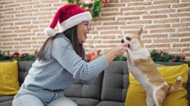 Chihuahua köpeği olan genç İspanyol kadın evde Noel şapkası takıyor.