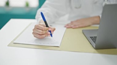Genç kızıl saçlı kadın klinikte laptopunu kullanarak tıbbi rapor yazıyor.