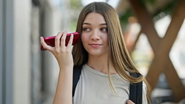 若いです美しいです女の子学生身に着けているバックパックリスニング音声メッセージによってスマートフォンでストリート — ストック動画