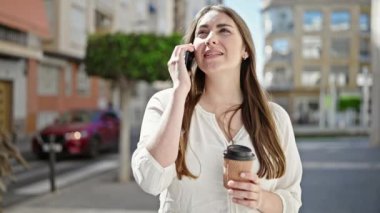 Genç, güzel, İspanyol bir kadın akıllı telefondan konuşuyor. Sokakta kahve içiyor.