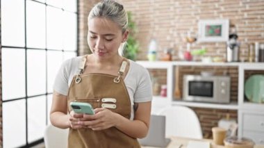 Yemek salonunda akıllı telefon kullanan önlük giyen güzel İspanyol bir kadın.