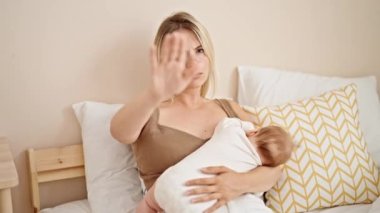 Anne ve kızı bebek emzirmek için yatakta oturuyorlar. Yatak odasında jest yapıyorlar.