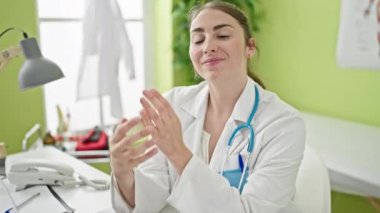 Klinikte kollarını kavuşturup masaya oturan genç, güzel İspanyol kadın doktor.