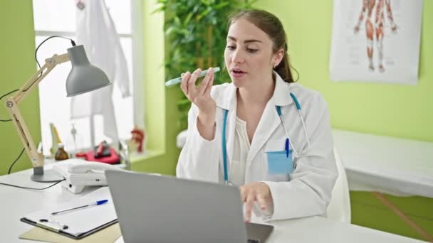 年轻美丽的惊慌失措的女医生在诊所用手提电脑用智能手机发送语音讯息 — 图库视频影像