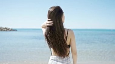 Mayolu genç Çinli kadın turist, deniz kenarında elleriyle saçlarını tarıyor.