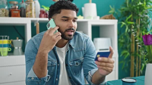 アフリカ系アメリカ人男性スマートフォンで話しているクレジットカードを持ってテーブルの上に座っているダイニングルーム — ストック動画