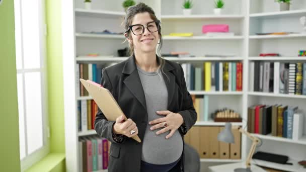 Młoda Ciężarna Kobieta Nauczyciel Trzymając Schowek Dotykając Brzucha Uniwersytecie Biblioteki — Wideo stockowe