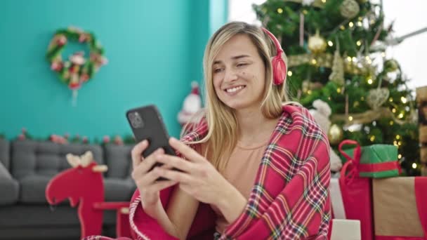 Mladá Blondýna Žena Pomocí Smartphone Sluchátka Slaví Vánoce Doma — Stock video