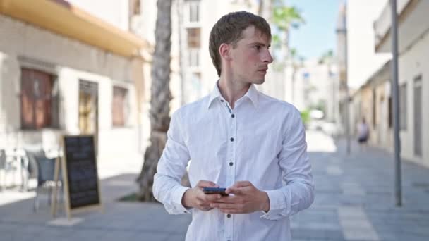 Junger Kaukasier Benutzt Smartphone Mit Ernster Miene Auf Der Straße — Stockvideo