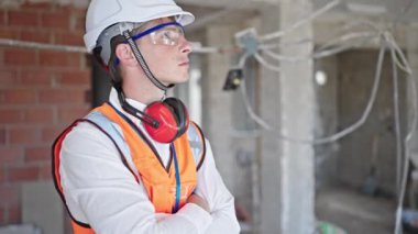 Kafkasyalı genç bir mimar inşaat alanında kolları çapraz hareket ve ciddi bir ifadeyle duruyor.