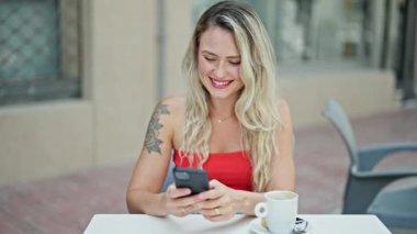 Kahve dükkanının terasında akıllı telefon kullanan genç sarışın kadın.
