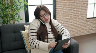 Genç, güzel İspanyol kadın dokunmatik ped kullanıyor. Evde akıllı telefondan konuşuyor.