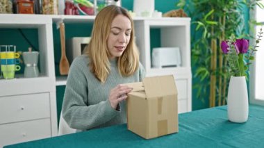 Genç sarışın kadın yemek odasında karton kutuları açıyor.