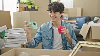 Genç İspanyol adam akıllı telefondan video izliyor. Yeni evinde kahve içiyor.