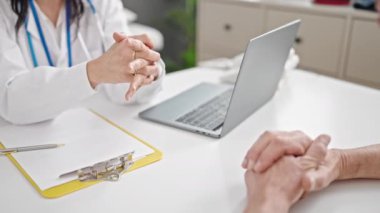Kıdemli erkek ve kadın doktor ve hasta klinikte laptoplarına bakıyorlar.