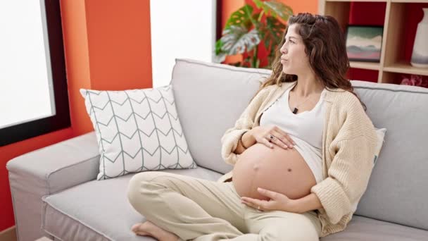 若いです妊娠中の女性座っています上のソファマッサージ腹ホーム — ストック動画