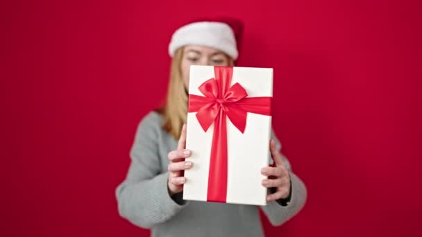 Jong Blond Vrouw Glimlachen Zelfverzekerd Holding Kerstcadeau Geïsoleerde Rood Achtergrond — Stockvideo