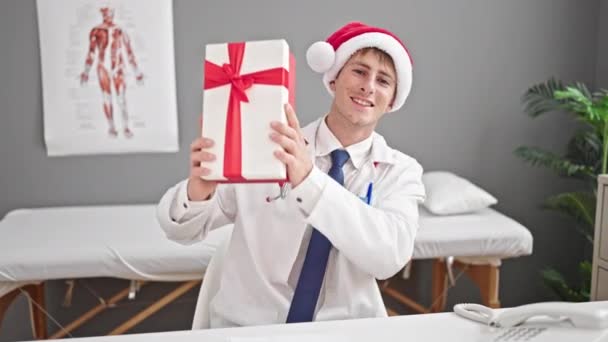 若いですCaucasian男医師保持クリスマスギフトでクリニック — ストック動画