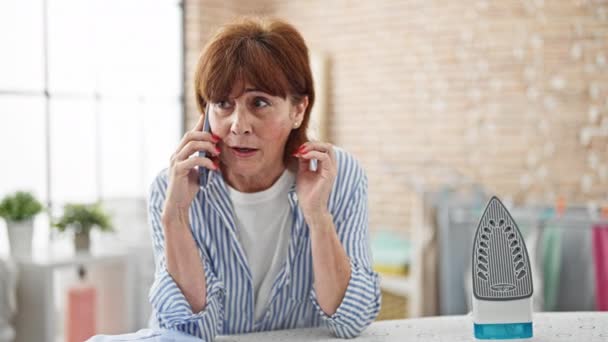 Mujer Mediana Edad Hablando Teléfono Inteligente Apoyado Tabla Planchar Sala — Vídeos de Stock