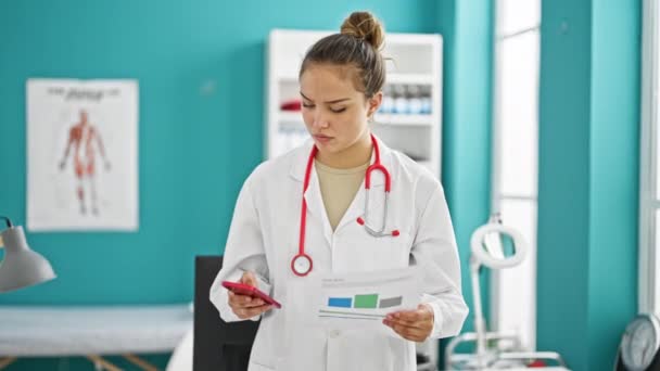 年轻美丽的惊慌失措的女医生在诊所用智能手机轻松地阅读医疗报告 — 图库视频影像