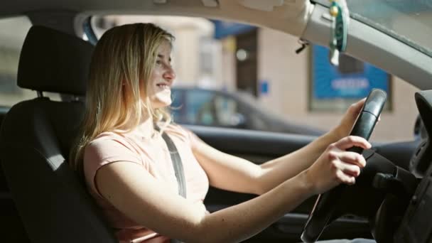 年轻的金发女人微笑着 自信地开车在街上 — 图库视频影像