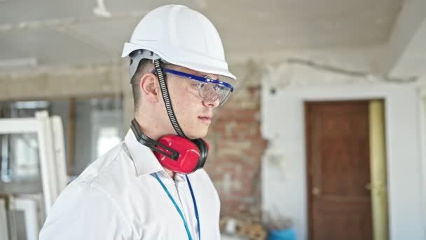 建設現場でリラックスした表情で立ってヘッドフォンを身に着けている若いヒスパニック系の男の建築家 — ストック動画
