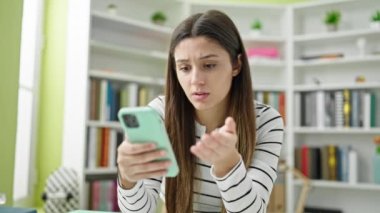 Akıllı telefon kullanan güzel İspanyol kız öğrenci kütüphane üniversitesine üzgün bakıyor.