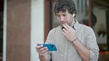 Genç İspanyol adam akıllı telefondan futbol maçı izliyor ve sokakta birinci sınıf jest yapıyor.