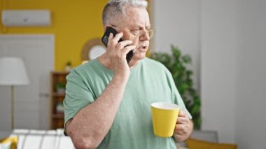 Orta yaşlı, kır saçlı, kahve içen, akıllı telefondan konuşan bir adam.
